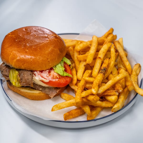 A burger with lettuce, tomato, and pickles next to a pile of golden french fries.