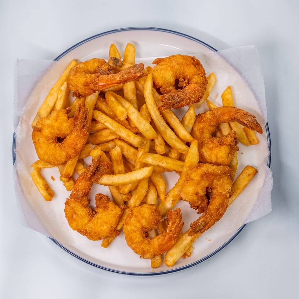 A white plate filled with golden-brown fried shrimp and french fries on a white background.
