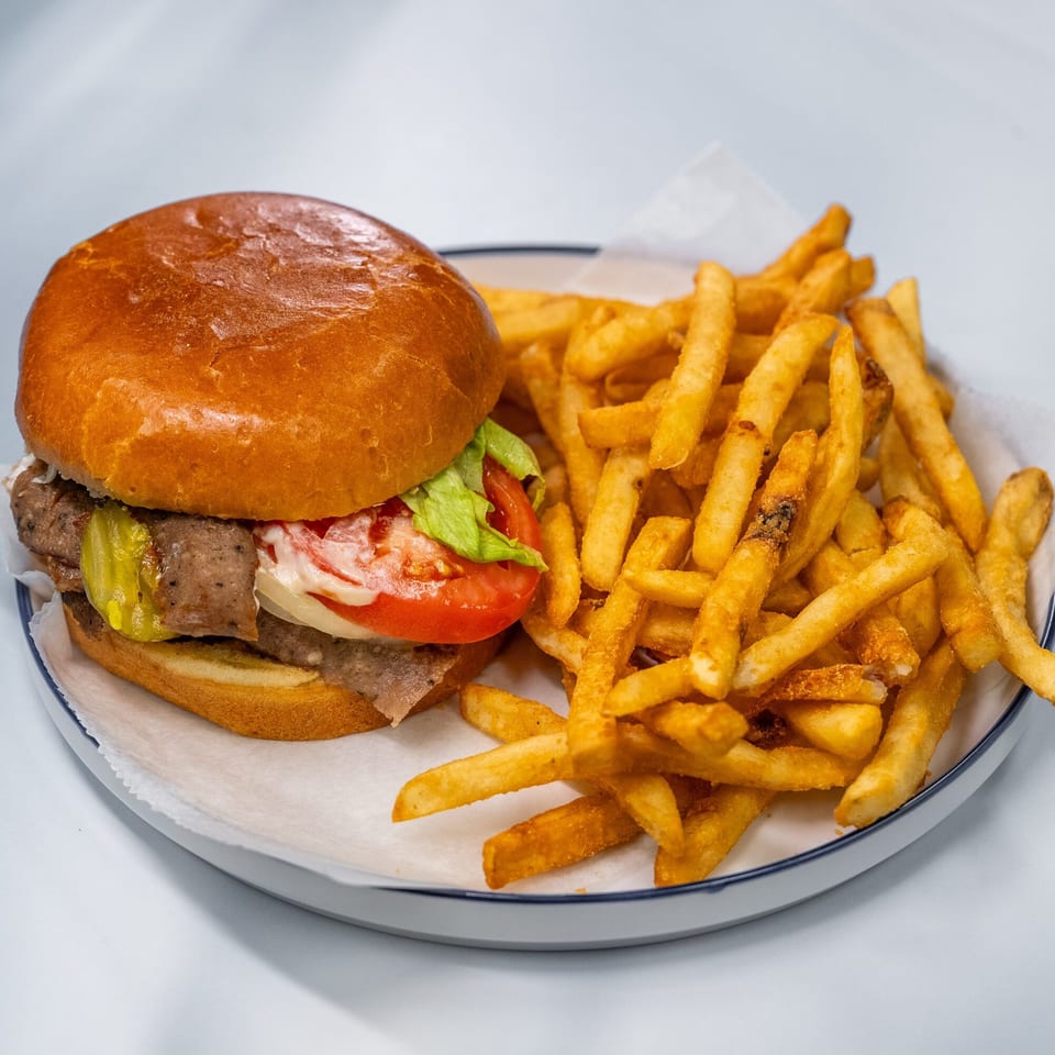 A Sharks Fish & Chicken burger with lettuce, tomato, pickles, and fries on a white plate.