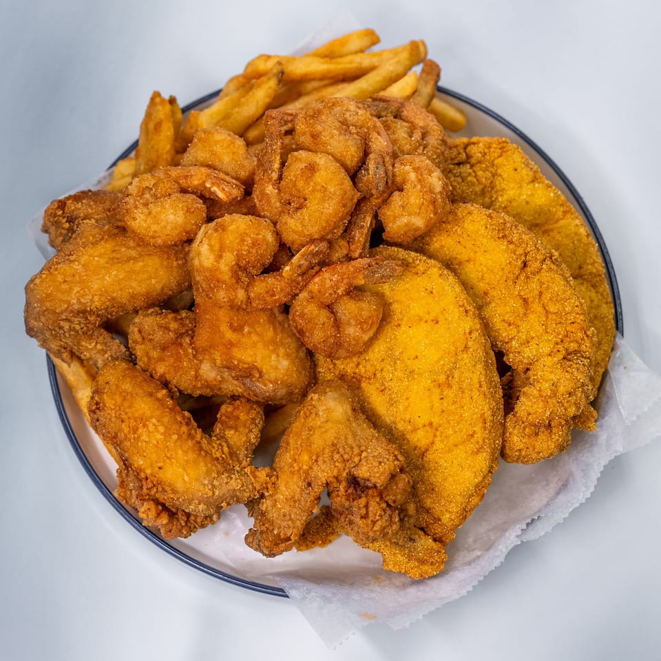 A platter of golden-fried shrimp, fish fillets, chicken wings, and french fries on white parchment paper.