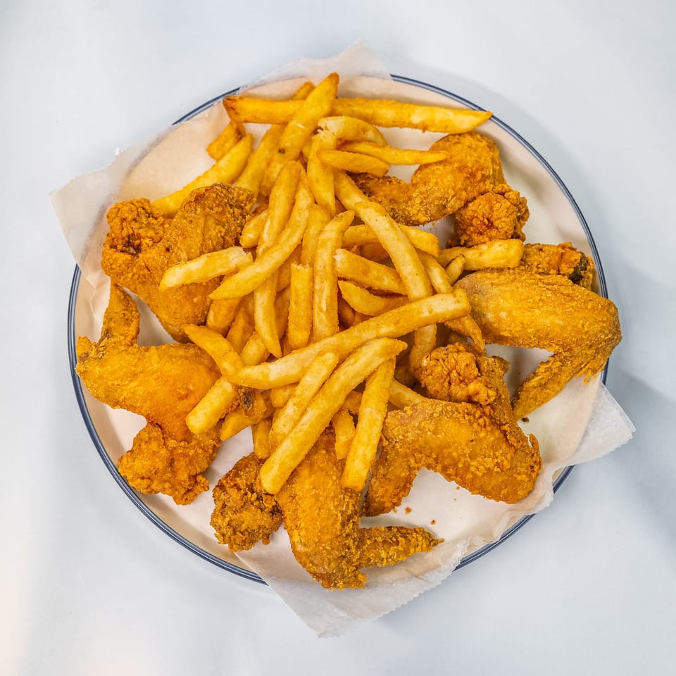 Crispy fried chicken wings and golden french fries served on a white plate with parchment paper.