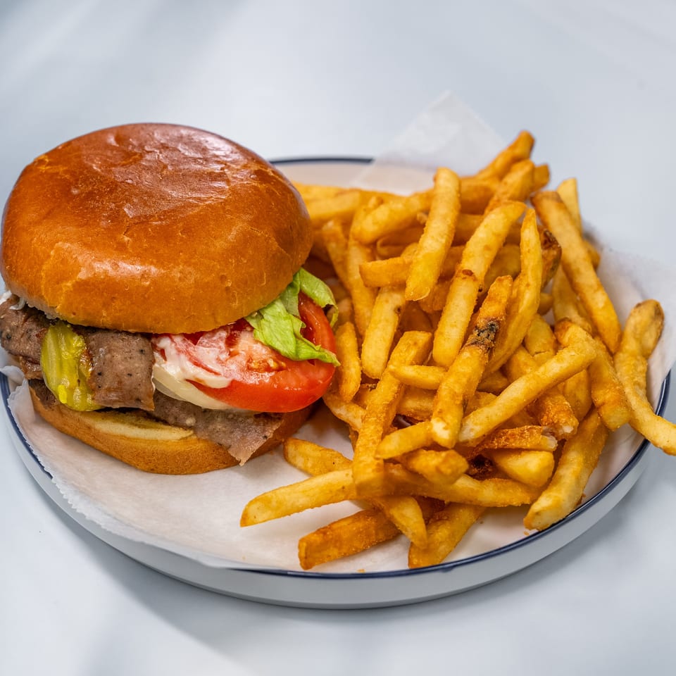 A beef burger with lettuce, tomato, onion, and pickles, served with a side of golden fries.