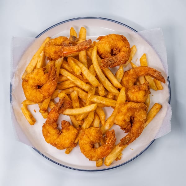A white plate of golden-brown fried shrimp and french fries, with parchment paper lining.