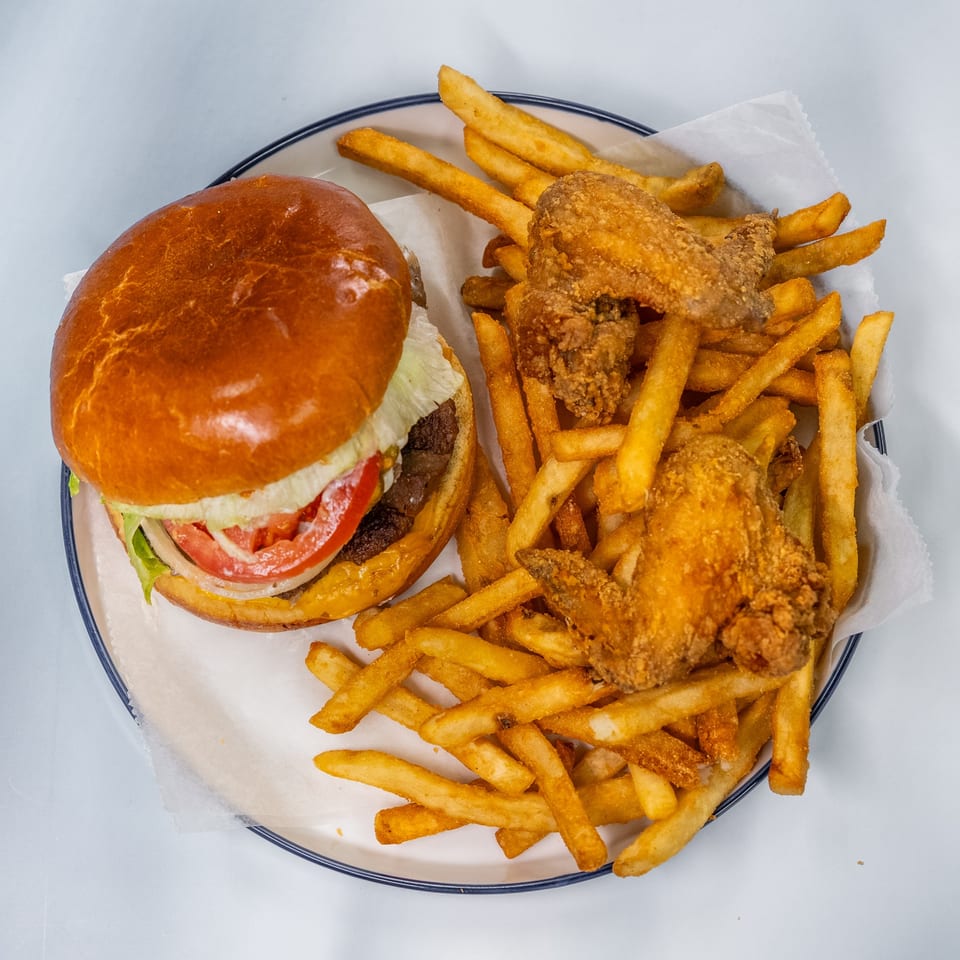 A cheeseburger with lettuce, tomato, and onion, served with crispy fries and fried chicken wings.