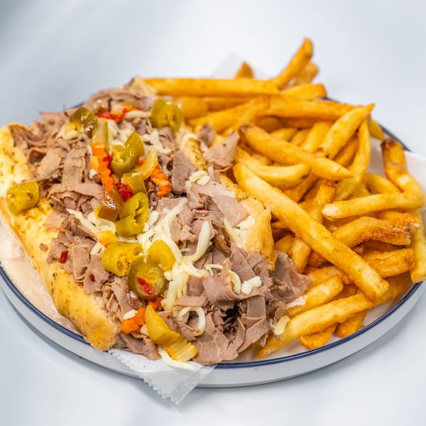 A Philly cheesesteak sandwich with peppers and onions, served with a side of golden french fries.