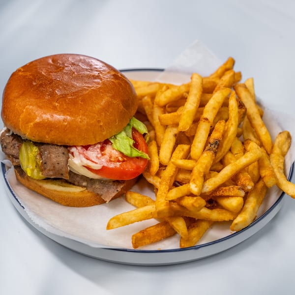 A beef sandwich with lettuce, tomato, and pickles, served with a side of golden french fries.