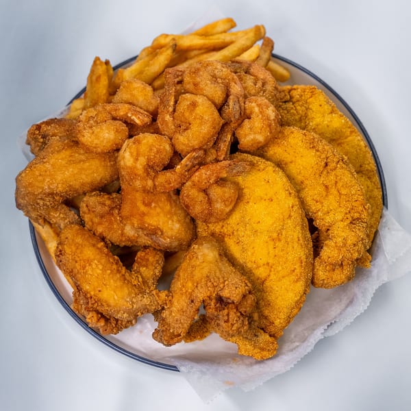 A platter of golden-brown fried chicken wings, shrimp, fish, and french fries from Sharks Fish & Chicken.